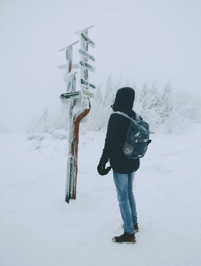 A hiker in winter attire checks frosted signs on a snowy trail, embodying adventure and exploration.